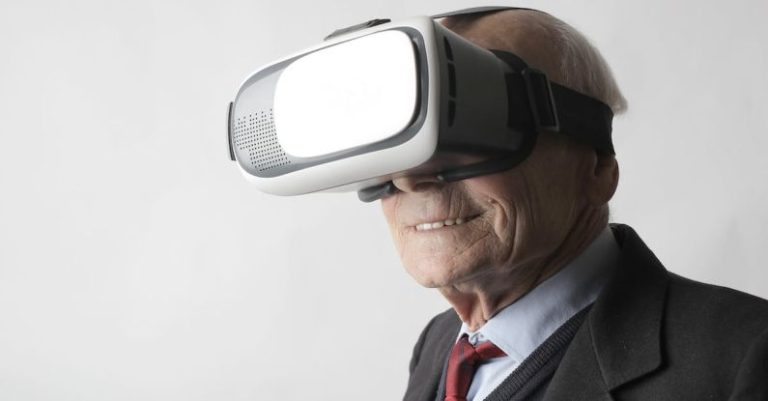 Wearables - Smiling elderly gentleman wearing classy suit experiencing virtual reality while using modern headset on white background